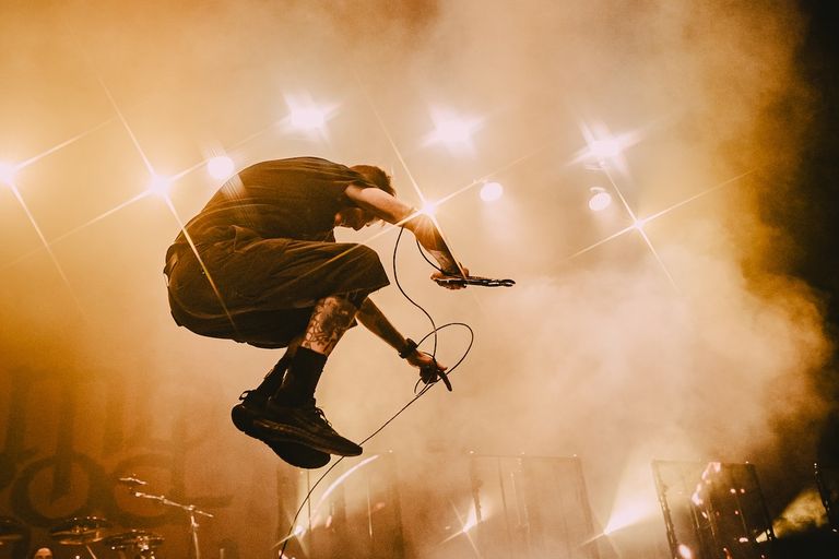 Lamb of God vocalist Randy Blythe captured mid-air leaping on stage during a high-energy heavy metal concert under dramatic stage lights